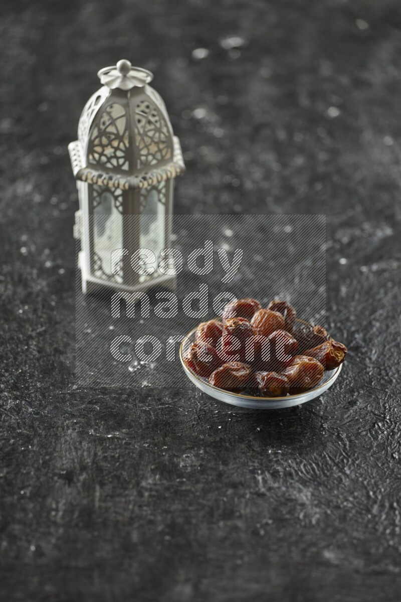 A white lantern with different drinks, dates, nuts, prayer beads and quran on textured black background