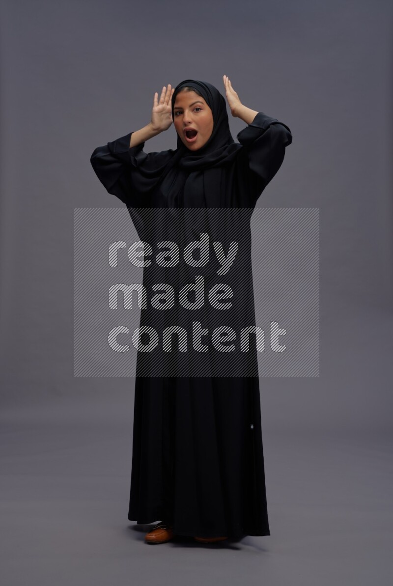 Saudi woman wearing Abaya standing hands behind head on gray background