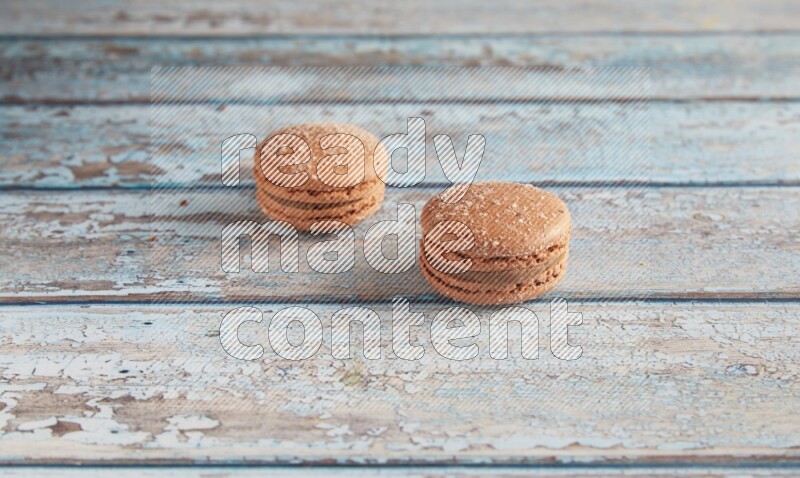 45º Shot of two Brown Hazelnuts macarons on light blue wooden background