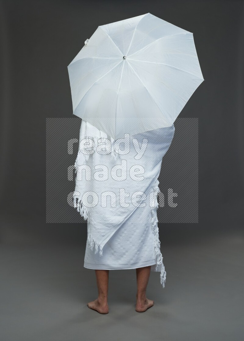 A man wearing Ehram Standing holding umbrella on gray background
