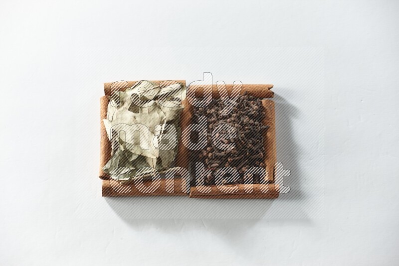 مربعان من أعواد القرفة ممتلئان بالقرنفل وأوراق الغار علي خلفية بيضاء