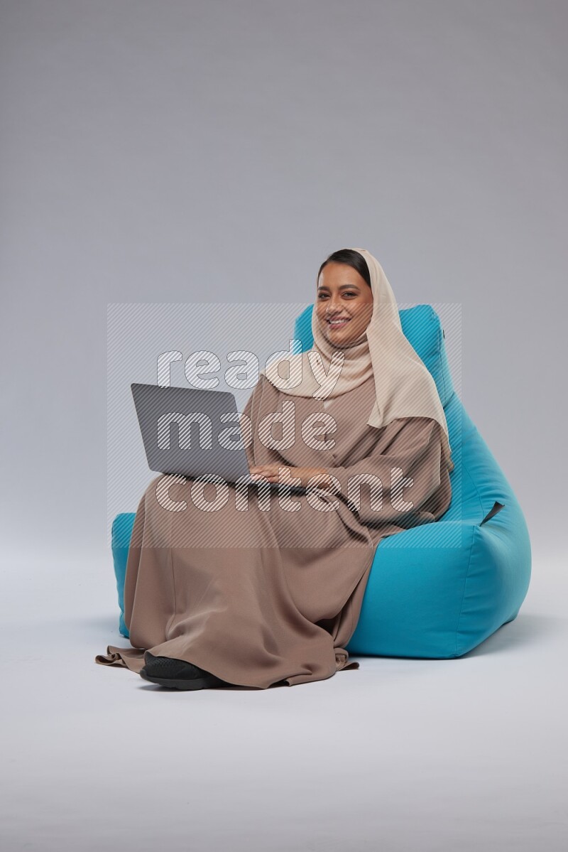 A Saudi woman sitting on a blue beanbag and working on laptop