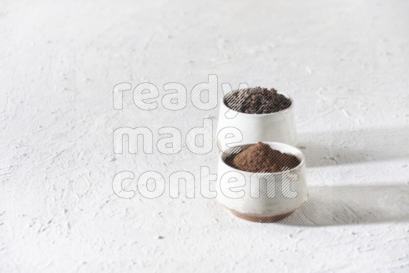 2 Beige ceramic bowls, one full of cloves and the other full of powder on textured white flooring