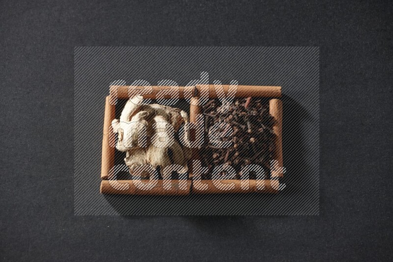 مربعان من أعواد القرفة ممتلئان بالقرنفل والزنجبيل المجفف علي خلفية سوداء