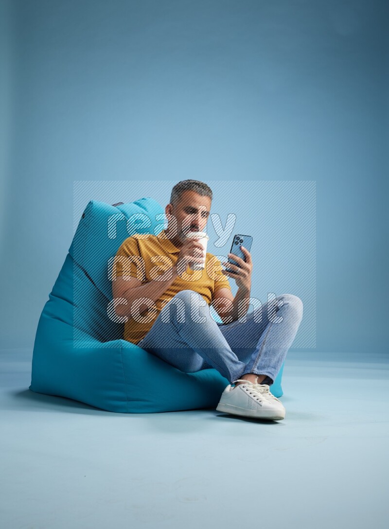 A man sitting on a blue beanbag and drinking coffee