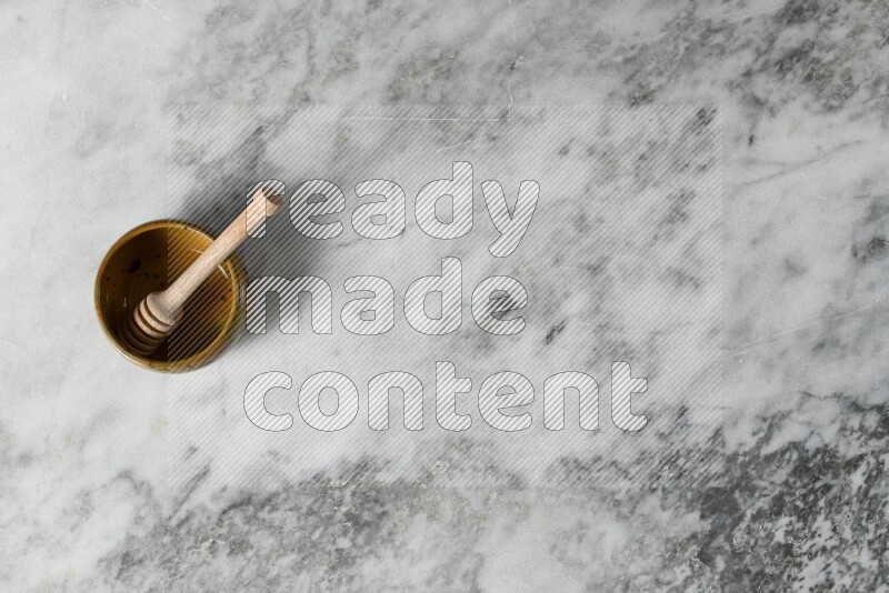 Multicolored pottery bowl with wooden honey dipper in it on grey marble background