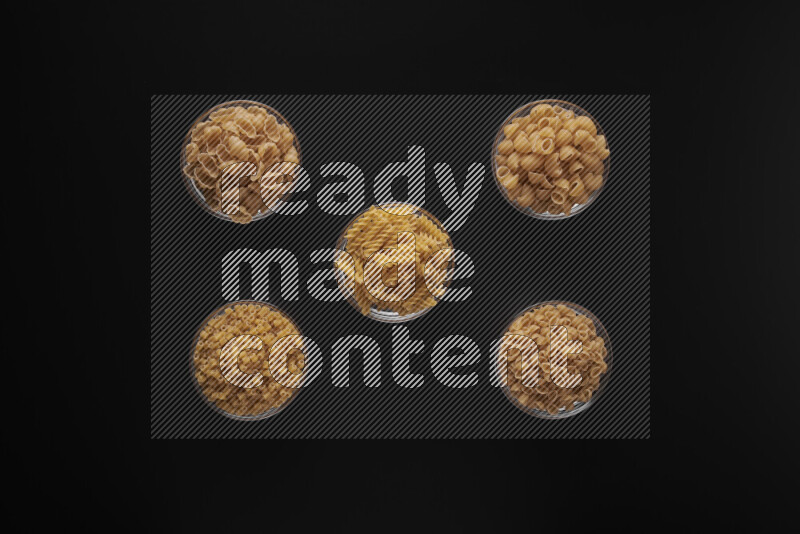 Different pasta types in 5 glass bowls on black background