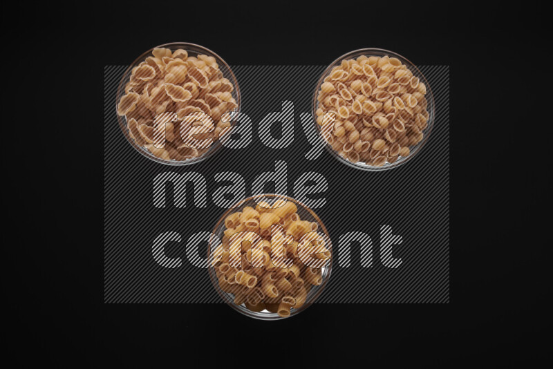 Different pasta types in glass bowls on black background