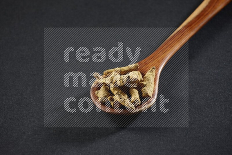 A wooden ladle full of dried turmeric fingers on black flooring