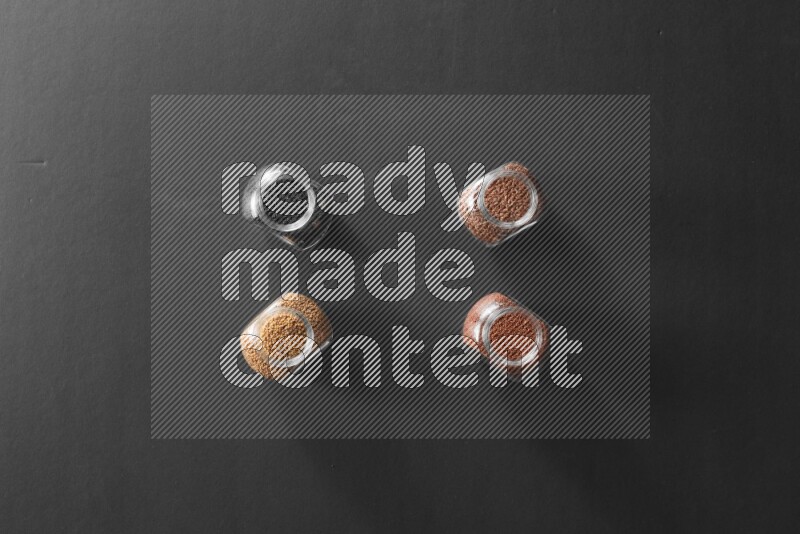 4 glass spice jars full of black seeds, mustard seeds, flax and garden cress on black flooring