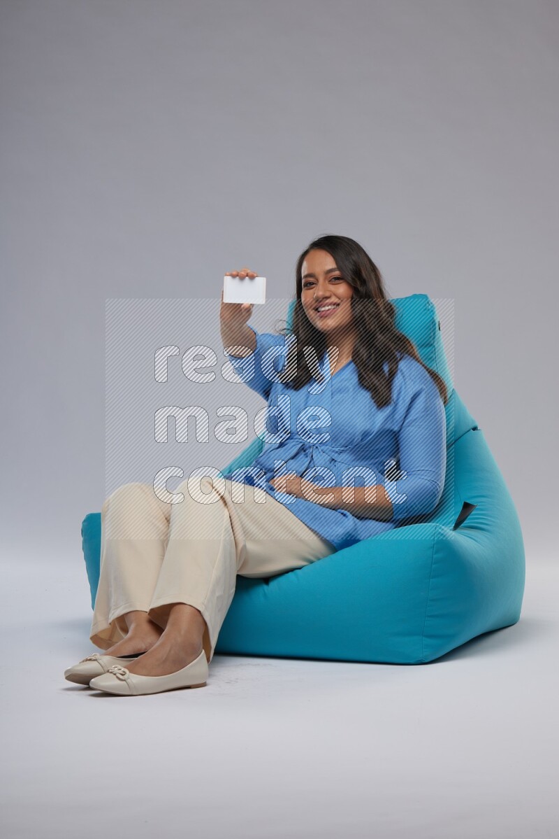 A woman sitting on a blue beanbag and holding ATM card