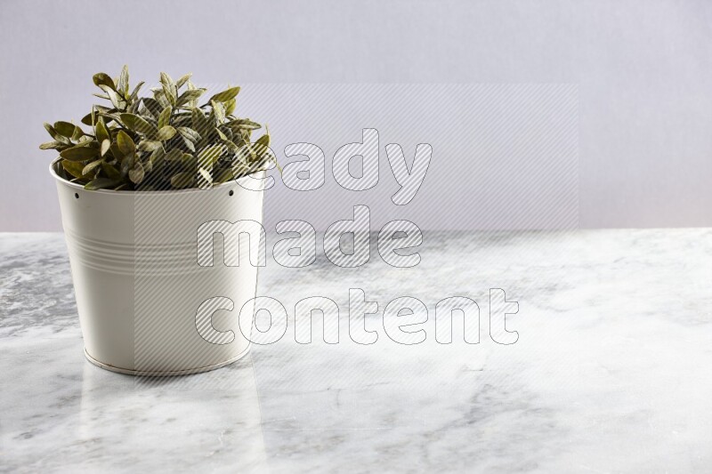 Green artificial plant in white pot on light grey marble background