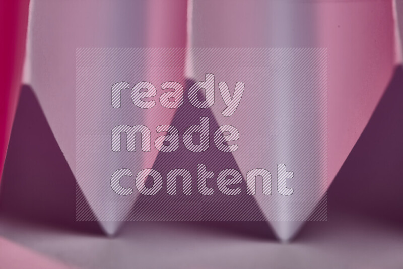 صورة مجردة مقربة تظهر طيات ورقية هندسية حادة بتدرجات اللون الوردي