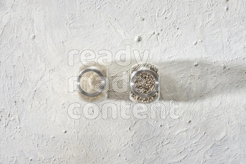 2 Herbal Glass jar full of white pepper beads and powder on textured white flooring