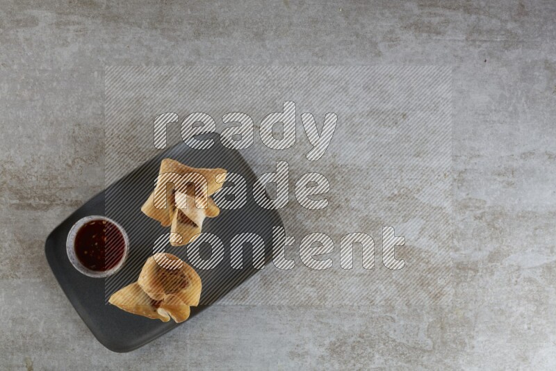 wonton cups with soy sauce ramkin on rectangle dark grey ceramic plate on grey textured counter top