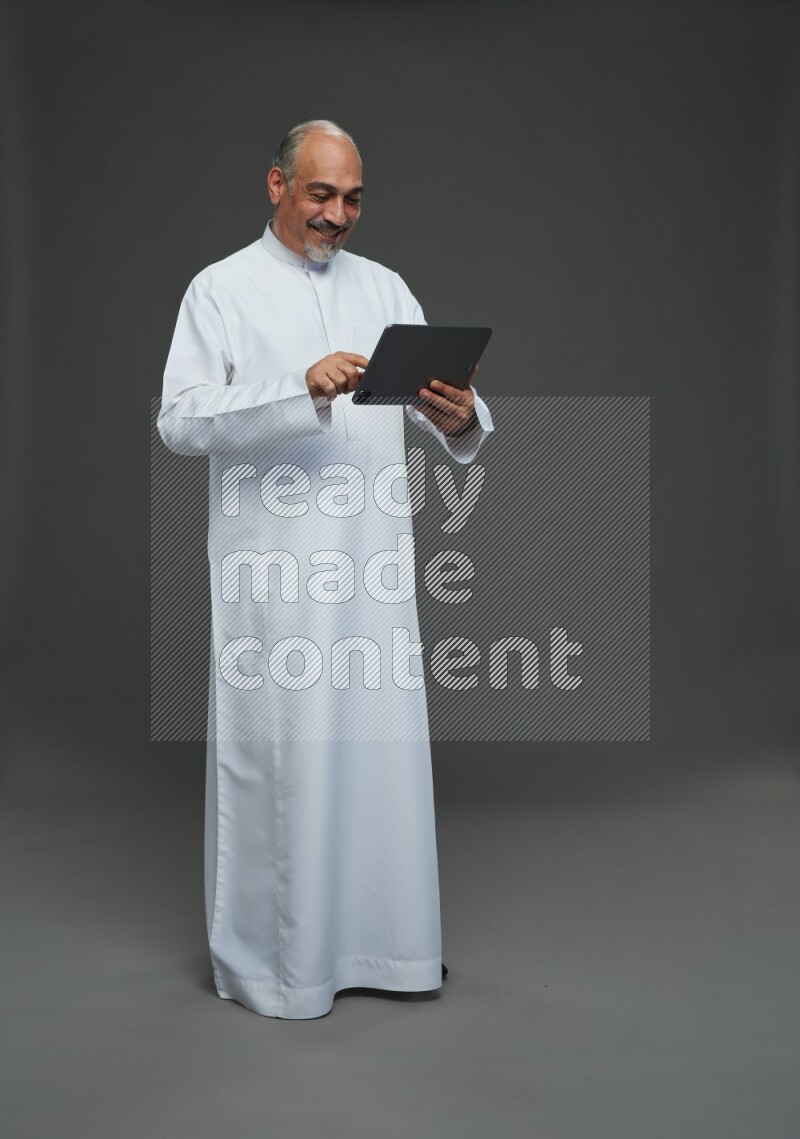 Saudi man without shomag Standing working on tablet on gray background