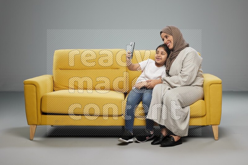 A girl sitting taking selfie with her mother on gray background