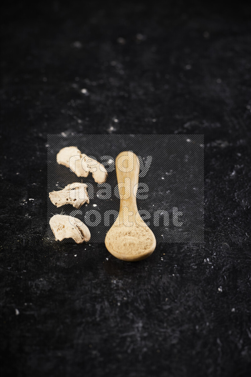 A wooden spoon full of ground ginger powder on black background