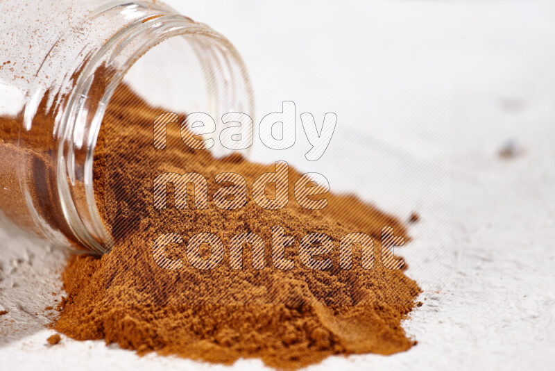 A glass jar full of ground paprika powder flipped with some spilling powder on white background