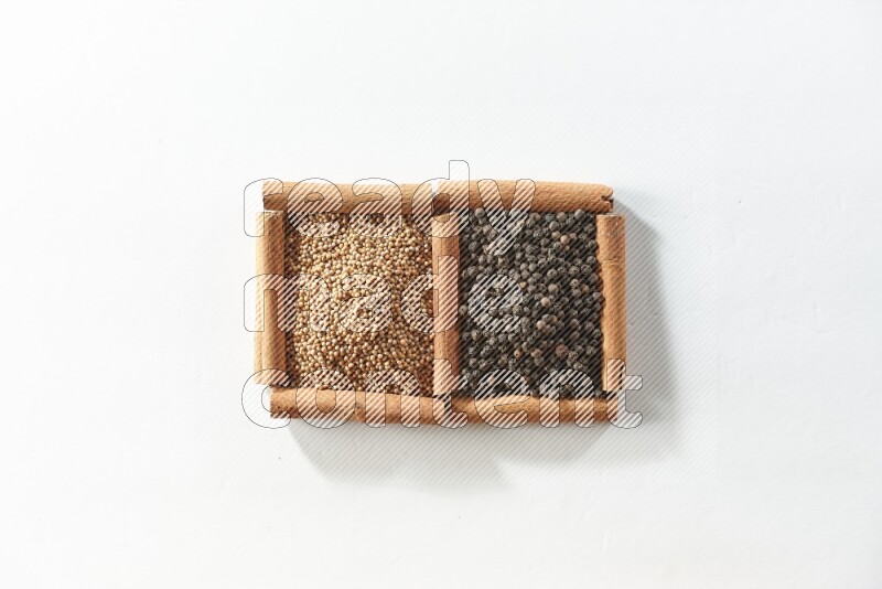 مربعان من أعواد القرفة ممتلئان بحبوب الخردل وحبوب الفلفل الأسود علي خلفية بيضاء