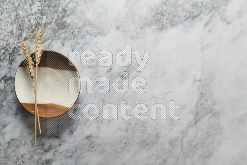 Wheat stalks on multicolored pottery plate on grey marble background