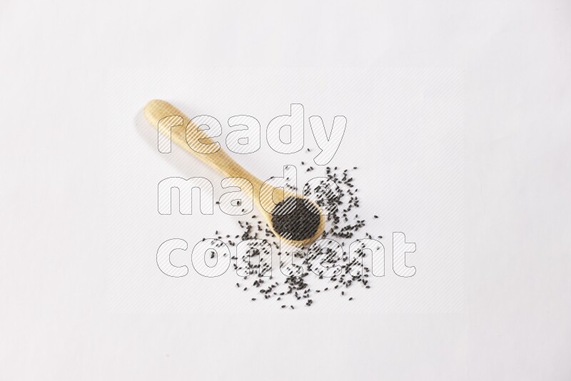 A wooden spoon full of black seeds on a white flooring