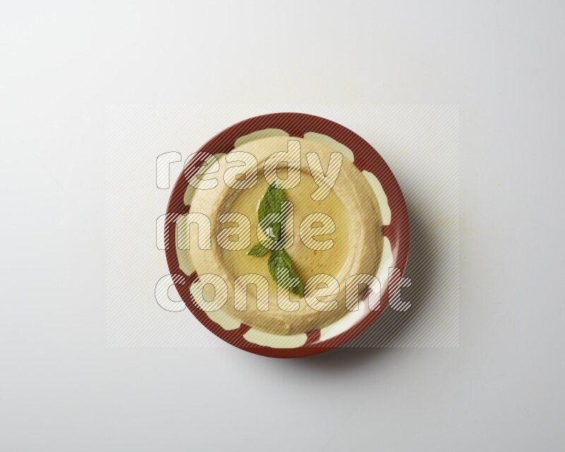 Hummus in a traditional plate garnished with mint on a white background
