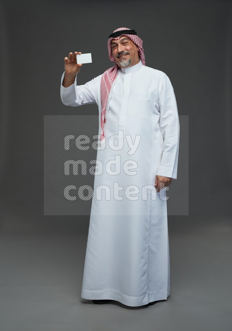 Saudi man with shomag Standing holding ATM card on gray background