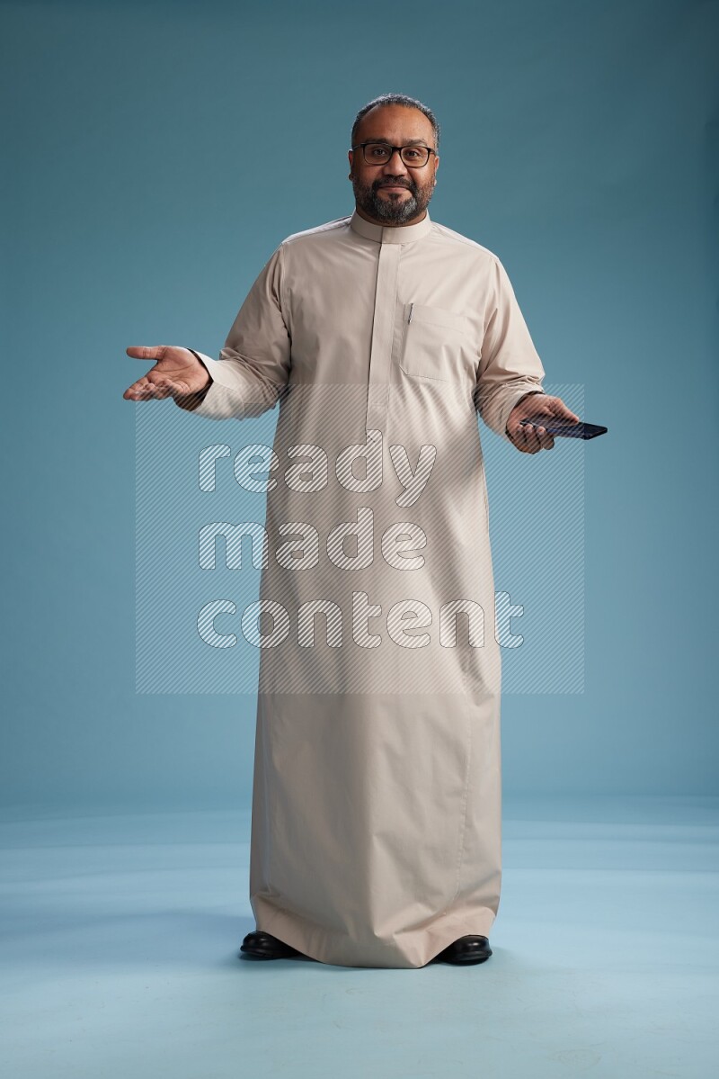 Saudi Man without shimag Standing texting on phone on blue background