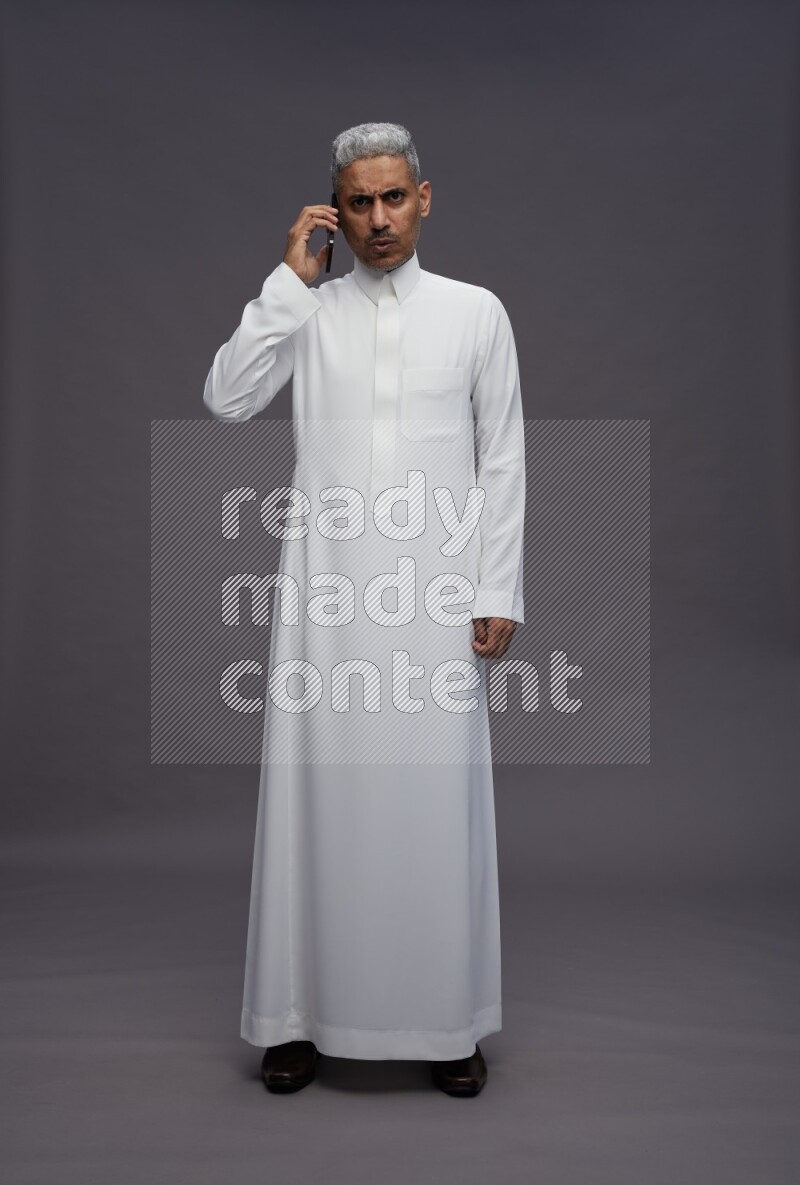 Saudi man wearing thob standing talking on phone on gray background