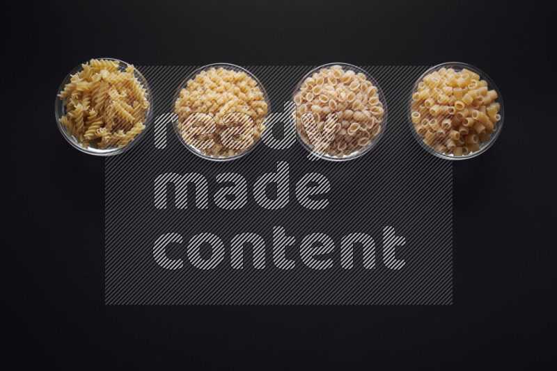 Different pasta types in glass bowls on black background