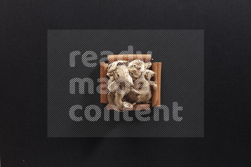 A single square of cinnamon sticks full of dried ginger on black flooring