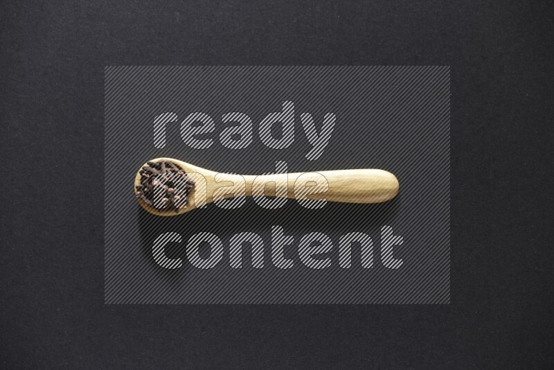 A wooden spoon full of cloves on a black flooring