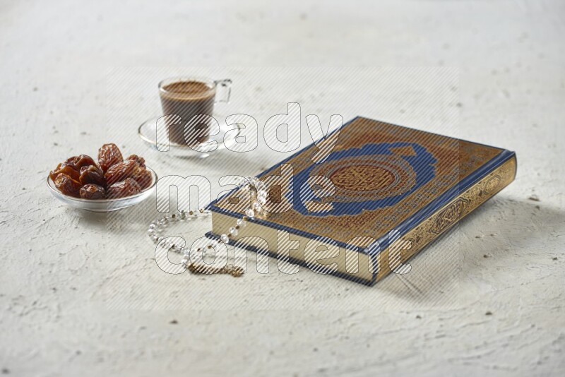 Quran with dates, prayer beads and different drinks all placed on textured white background