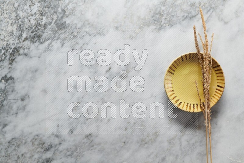 Wheat stalks on multicolored pottery plate on grey marble background