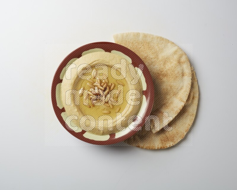 Hummus in a traditional plate garnished with pine nuts on a white background
