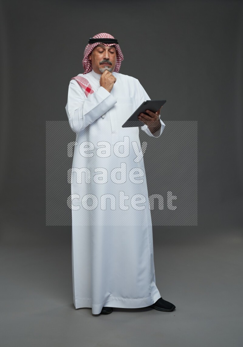 Saudi man with shomag Standing working on tablet on gray background