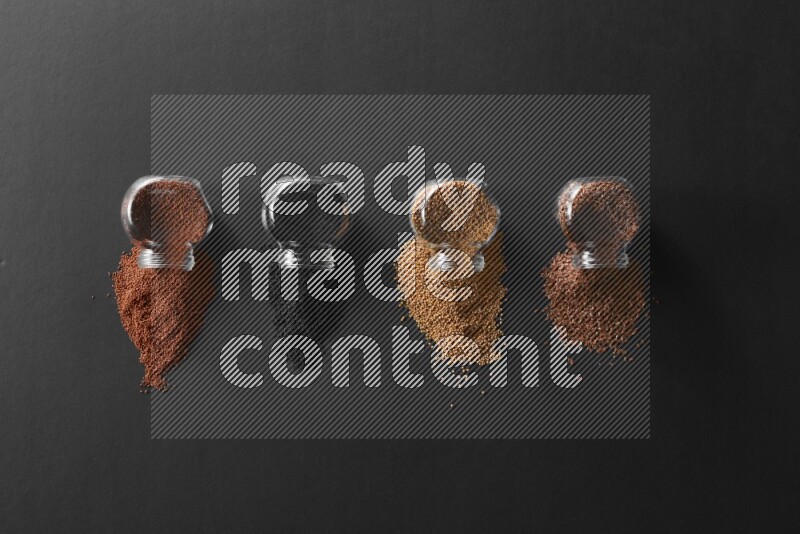 4 glass spice jars full of black seeds, mustard seeds, flax and garden cress on black flooring