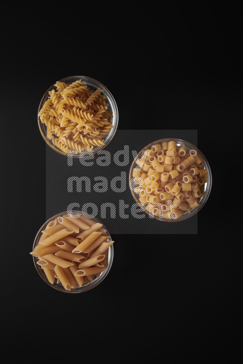 Different pasta types in glass bowls on black background