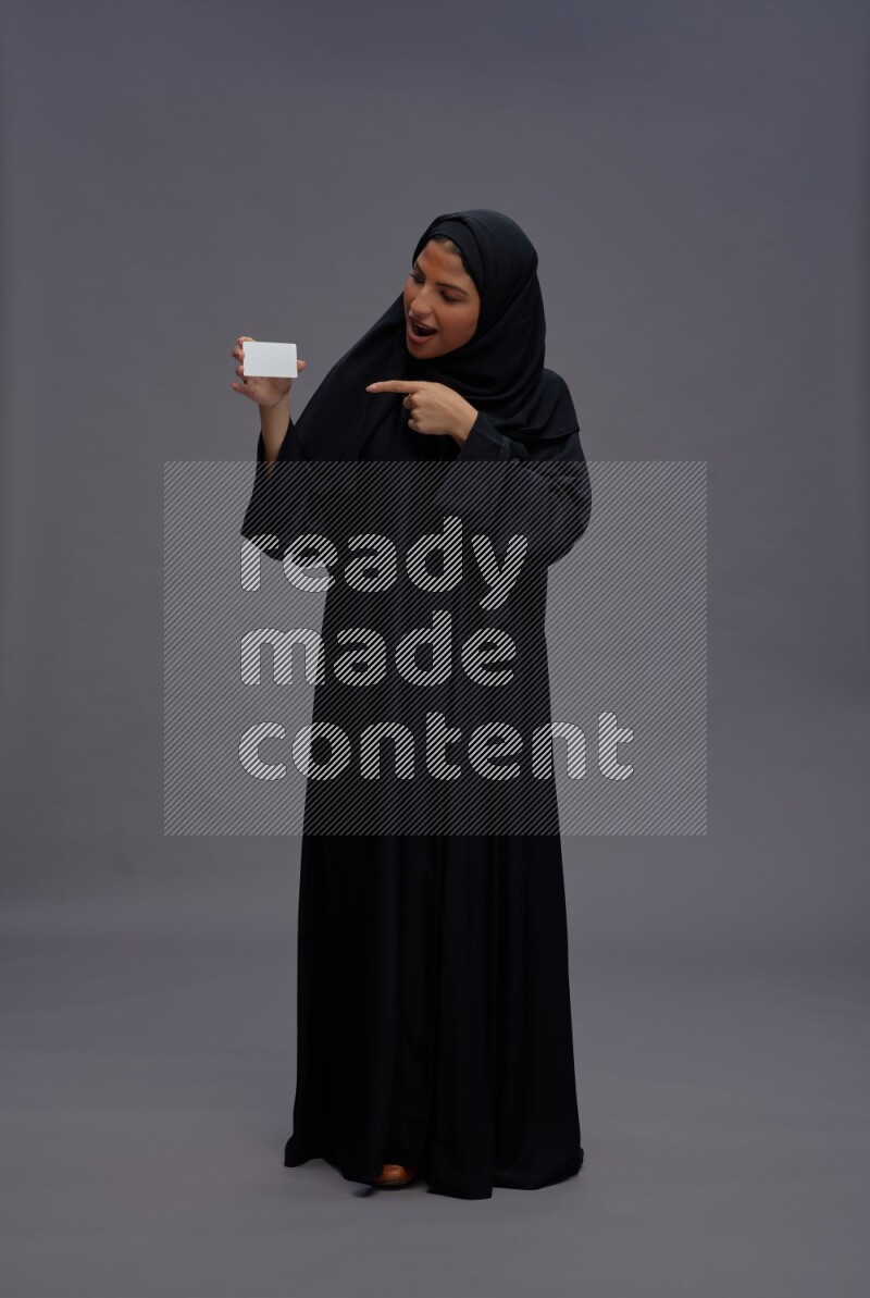 Saudi woman wearing Abaya standing holding ATM card on gray background