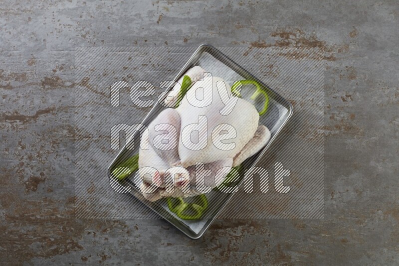 whole Raw chicken on a small oven trey direct on a rustic grey background
