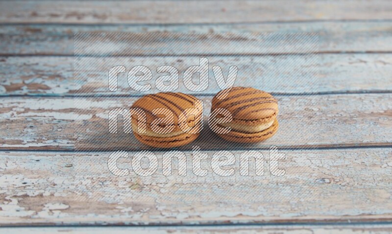 45º Shot of two light brown Almond Cream macarons on light blue wooden background