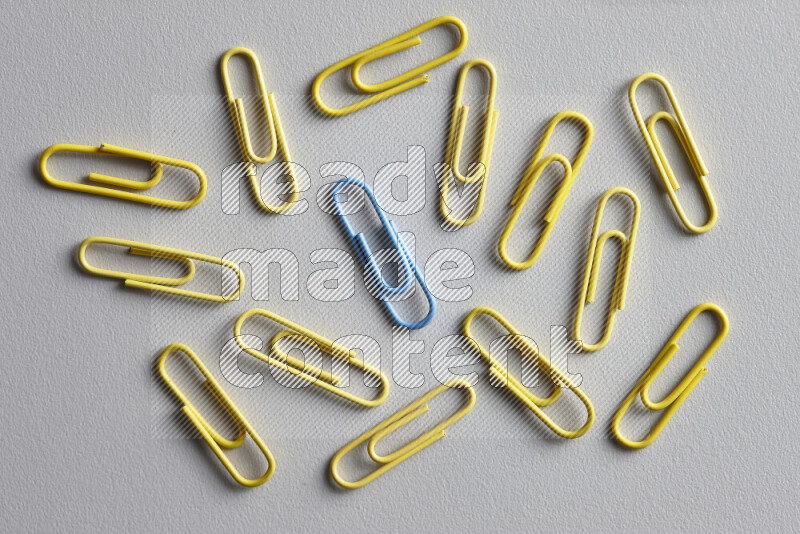 A bunch of yellow paper clips with a different colored paper clip in the center on grey background
