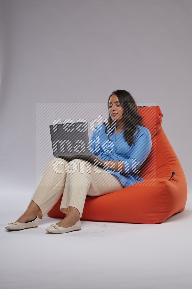 A woman sitting on an orange beanbag and working on laptop