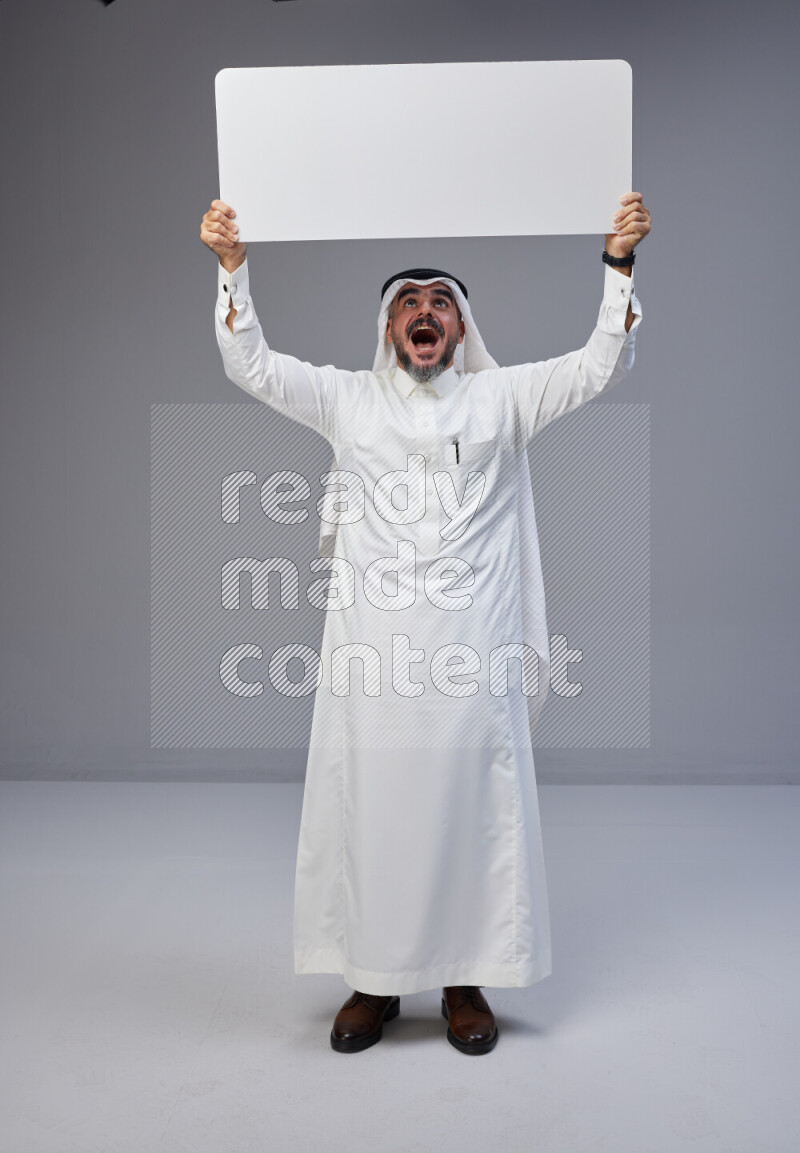 Saudi man Wearing Thob and white Shomag standing holding board on Gray background