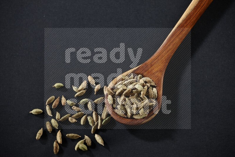 A wooden ladle full of cardamom on black flooring