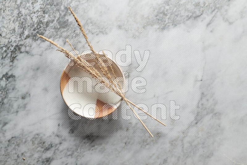 Wheat stalks on multicolored pottery plate on grey marble background