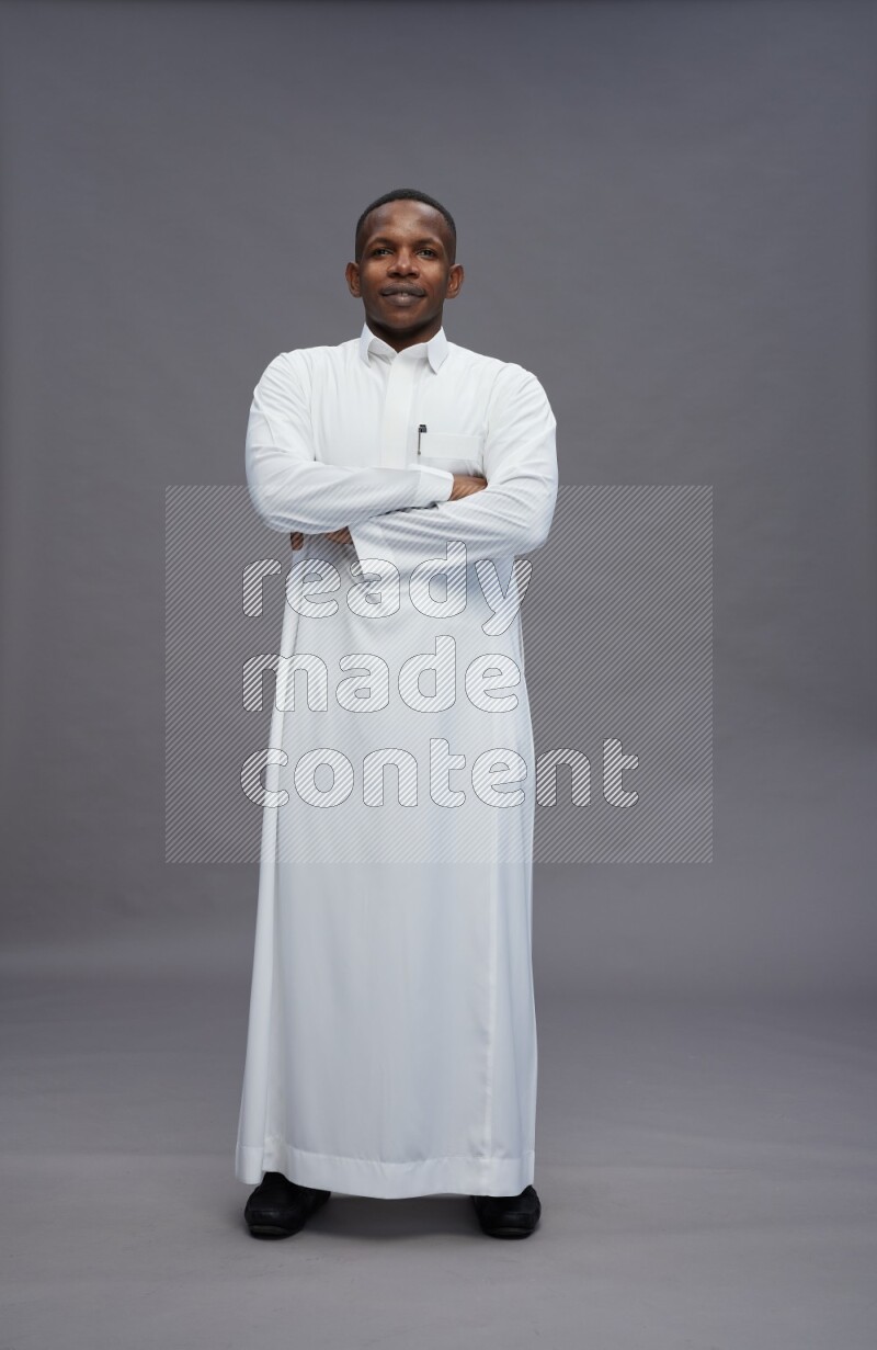 Saudi man wearing thob standing with crossed arms on gray background