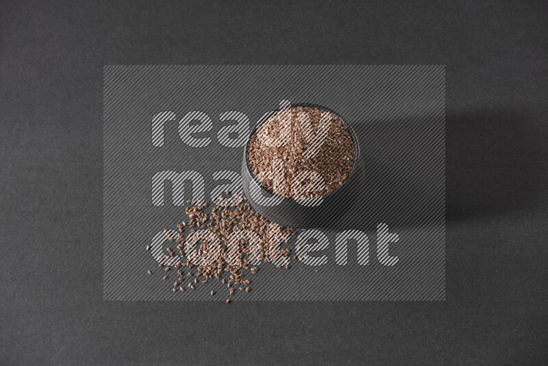 وعاء فخاري أسود ممتلئ بحبوب بذر الكتان محاط بالبذور على أرضية سوداء