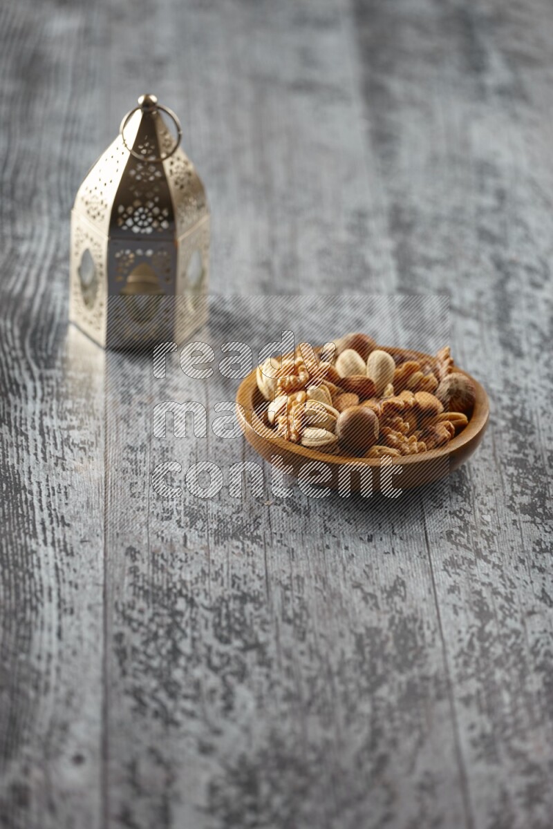 A silver lantern with different drinks, dates, nuts, prayer beads and quran on grey wooden background